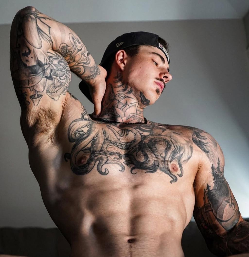 Tattooed male model flexing shirtless in a backwards cap — Best Male OnlyFans creator