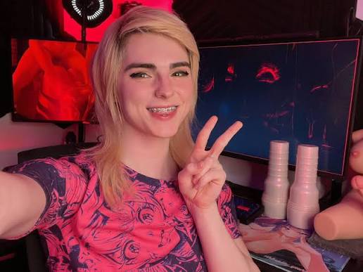 Blonde Femboy OnlyFans creator posing with a peace sign in front of a gaming desktop setup.