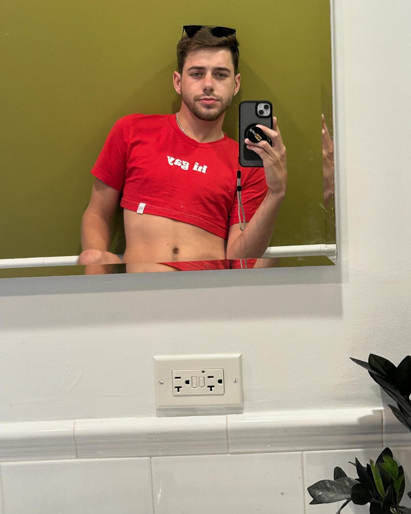 Man taking a bathroom mirror selfie in a red crop top — Best Male OnlyFans model