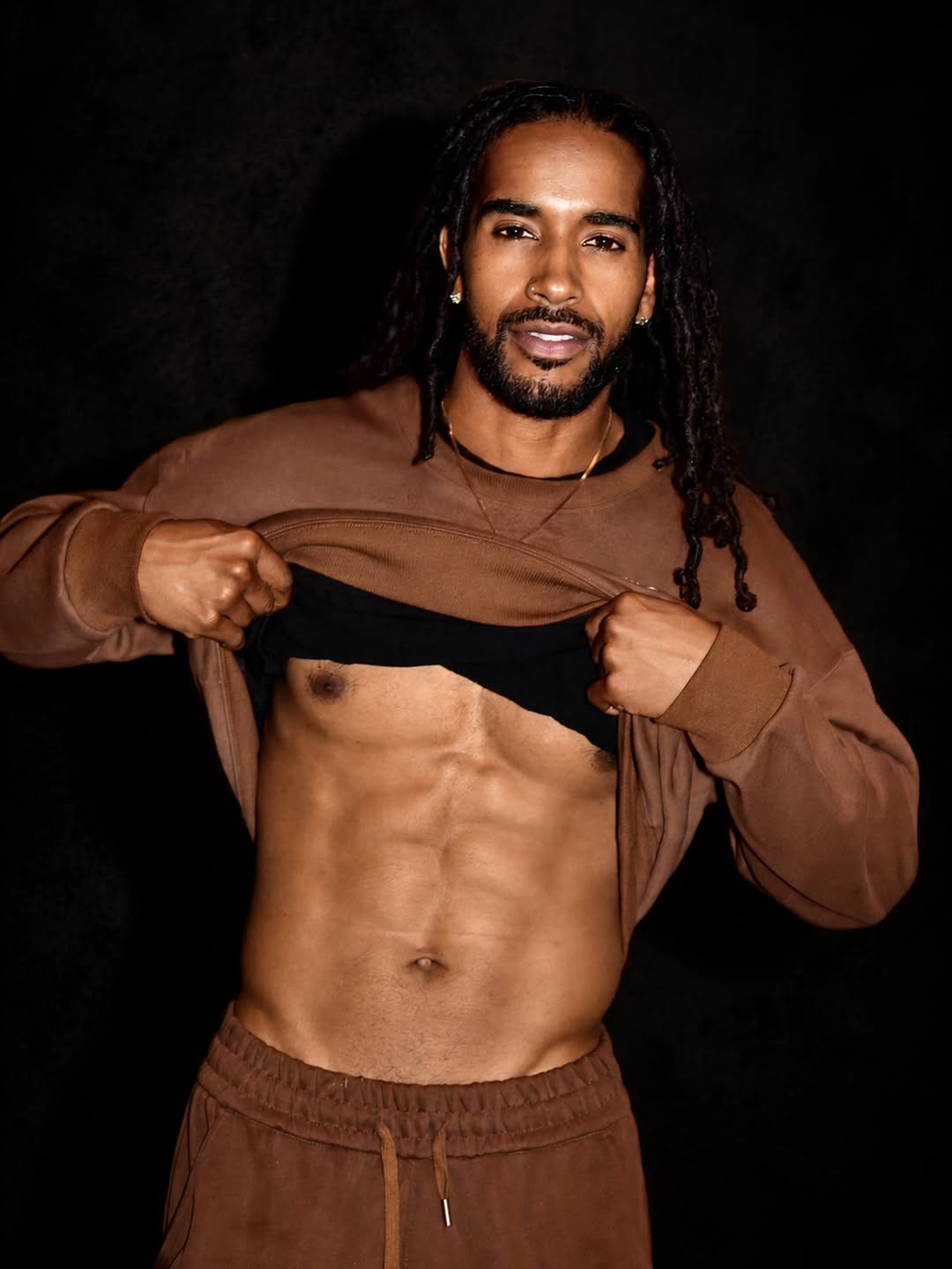 Fit creator with dreadlocks lifting his sweater against a dark background, tagged for best black onlyfans search.