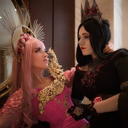 Top Convention Cosplayers featuring two women in elaborate fantasy costumes, one with a pink wig and sun halo crown, looking up at another with dark hair and a gothic crown