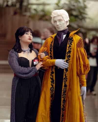 Top Convention Cosplayers featuring a woman in a dark corset dress standing beside a man cosplaying as Percy de Rolo with pale makeup and an ornate yellow coat