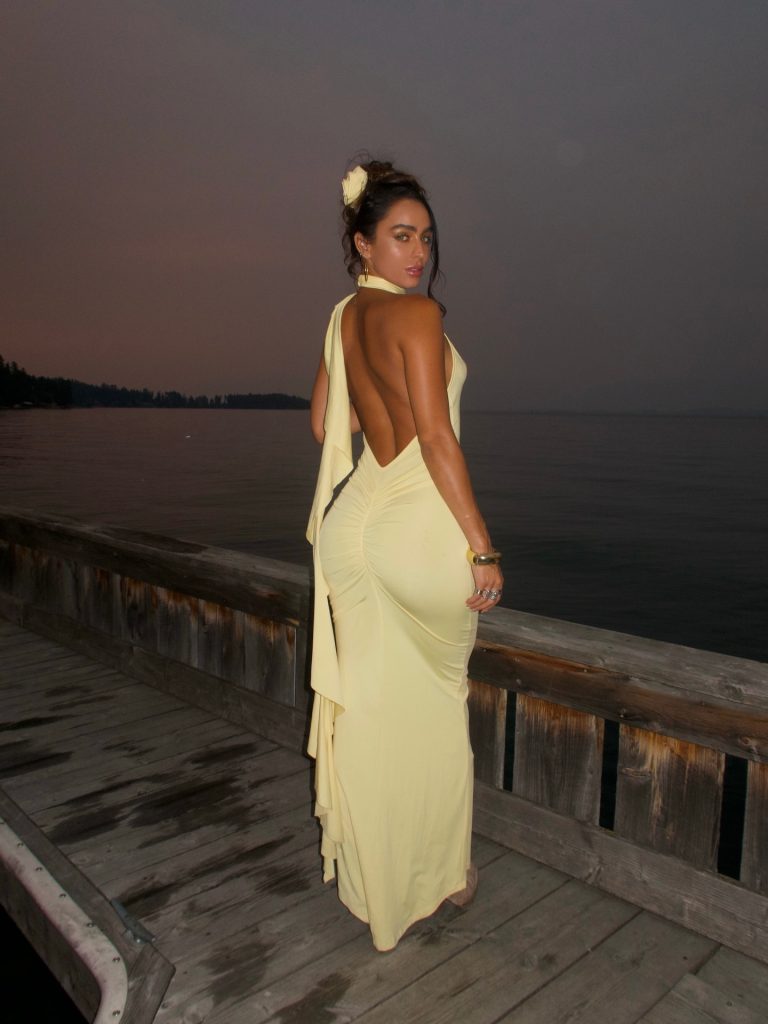 Fitness model Sommer Ray posing in a backless yellow evening gown on a wooden dock at sunset for Muscular Women OnlyFans search optimization.