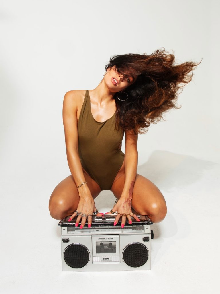 Fitness creator Sommer Ray kneeling over a vintage boombox in an olive green bodysuit