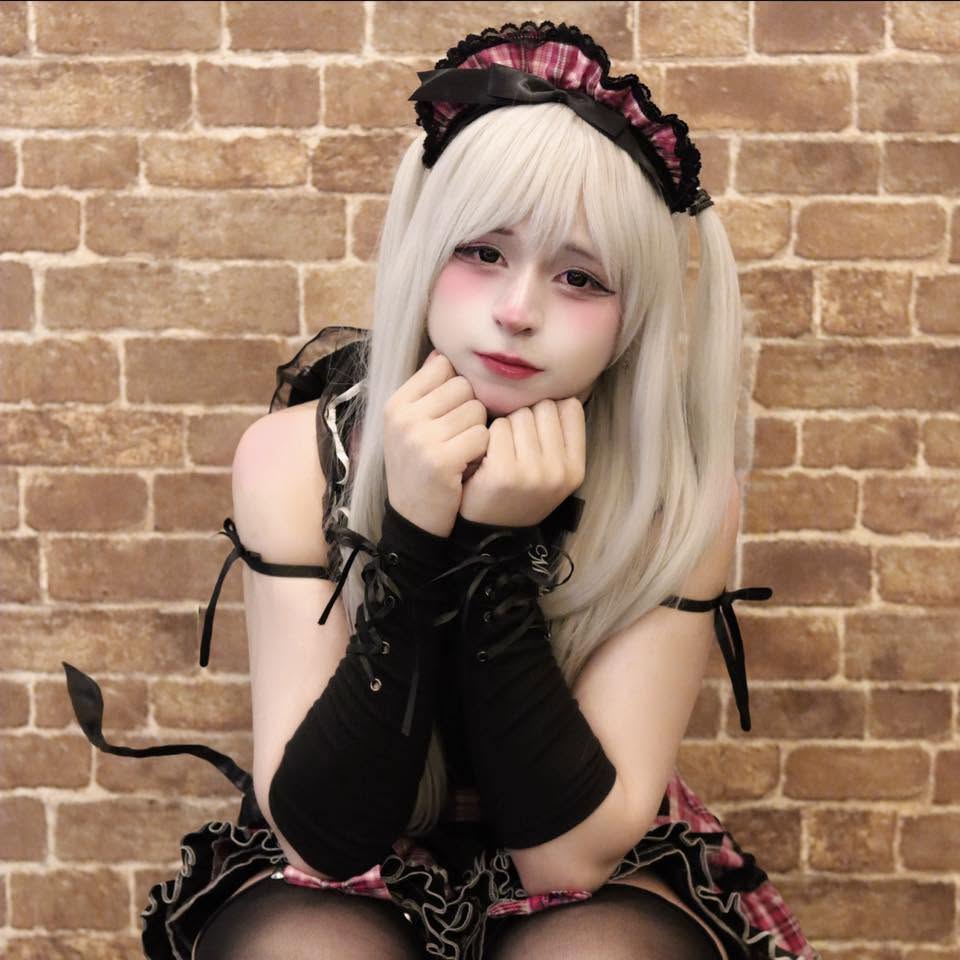Japanese cosplay Femboy OnlyFans creator in a blonde wig and maid outfit leaning on a brick wall.