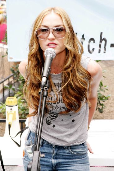 Drea de Matteo speaking at an outdoor microphone in sunglasses and a graphic tee, discussing the launch of her Drea De Matteo OnlyFans profile.