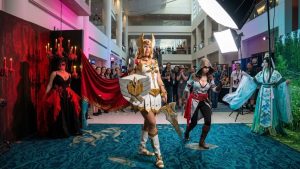 Top Convention Cosplayers posing together at a fan convention including She-Ra, an Assassin's Creed assassin, a gothic masquerade character, and a traditional Chinese fantasy character