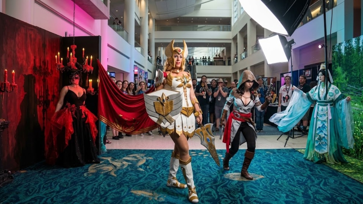Top Convention Cosplayers posing together at a fan convention including She-Ra, an Assassin's Creed assassin, a gothic masquerade character, and a traditional Chinese fantasy character