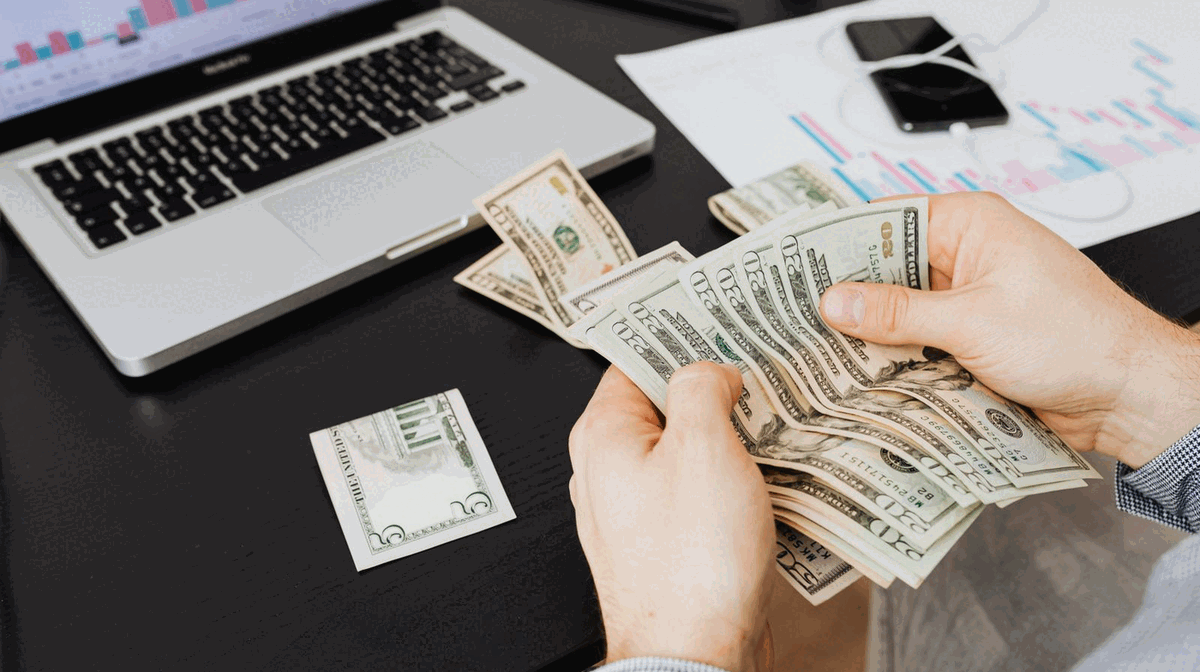 Creator counting OnlyFans earnings at a desk beside financial charts