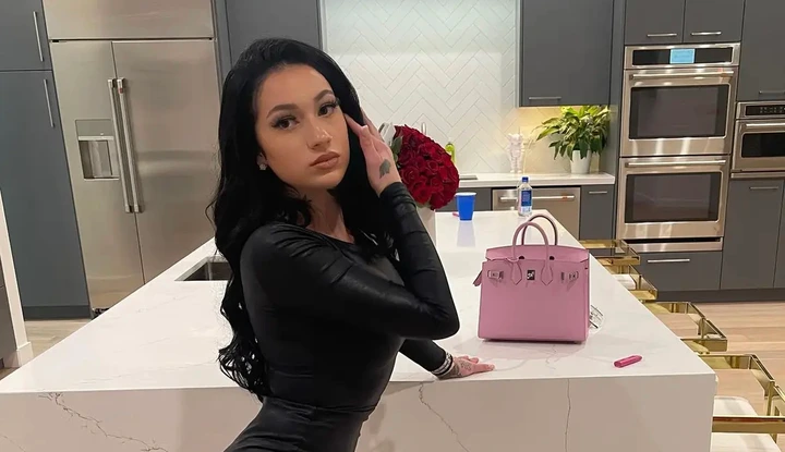 A portrait of influencer Bhad Bhabie posing in a modern kitchen, embodying the aesthetic of a Brat OnlyFans creator with her black dress and pink handbag