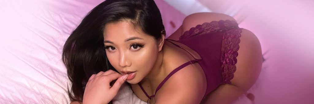 Numi Rias posing playfully in a burgundy lace bodysuit