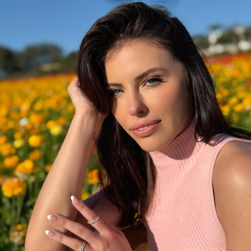 Adriana Chechik with dark hair in a pink sleeveless top posing in a field of yellow flowers – twitch streamers with onlyfans